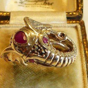 Peut inclure: Une bague en argent en forme d'éléphant avec des accents de rubis rouges et de pierres précieuses noires. La bague est dans une boîte doublée de velours.