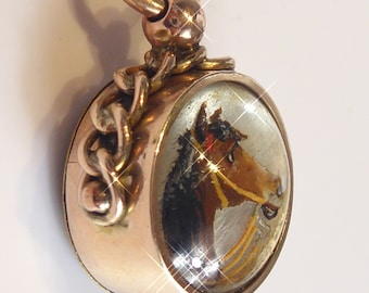 May include: A gold-toned pocket watch fob with a chain and a glass cover featuring a painted image of a horse's head.