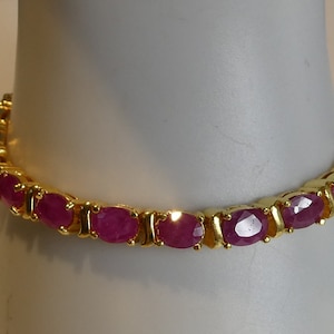 Könnte beinhalten: Ein goldenes Armband mit rosafarbenen ovalen Edelsteinen.