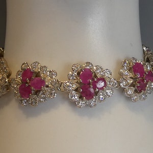May include: A silver bracelet featuring a cluster of pink gemstones surrounded by smaller white gemstones. The bracelet has a floral design.