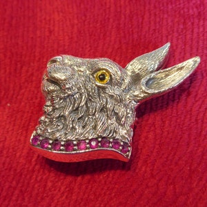 May include: A silver rabbit head brooch with a yellow eye and a row of pink gemstones around the neck.