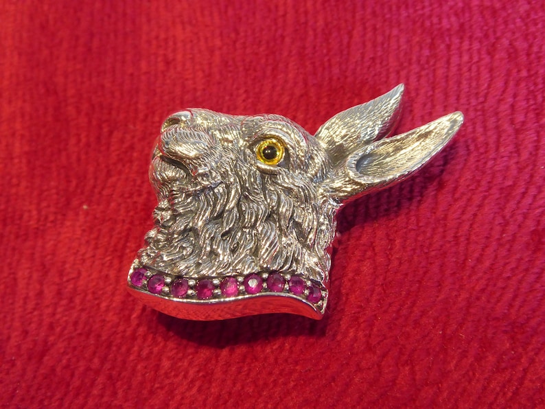 May include: A silver rabbit head brooch with a yellow eye and a row of pink gemstones around the neck.
