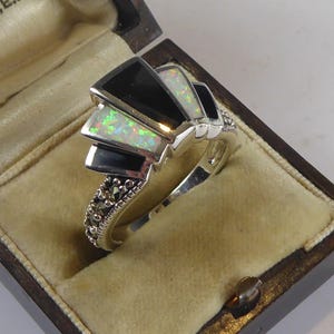 Op de afbeelding: Een zilveren ring met een zwarte en witte opaal-steen gezet in een geometrisch ontwerp. De ring is versierd met marcasiet-stenen.