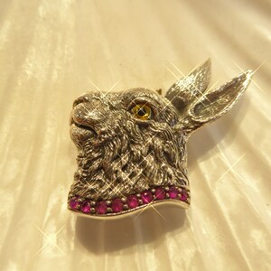 May include: A silver rabbit head brooch with a yellow eye and a row of pink gemstones around the neck.