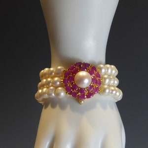 May include: A white pearl bracelet with a pink and gold flower-shaped clasp. The clasp is made of small pink stones set in gold.
