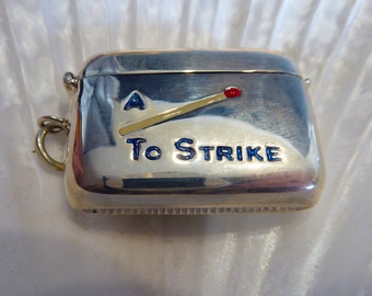 May include: A silver match safe with a blue and white enamel design of a matchstick with the text "To Strike".