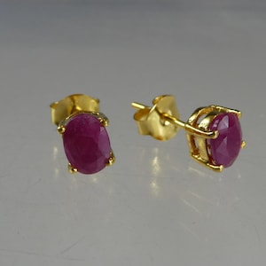 Pode incluir: Um par de brincos de tarracha com rubis de corte oval em um tom vermelho rosado profundo, montados em engastes de ouro de quatro garras. Cada brinco inclui um pino de ouro correspondente e uma tarracha de borboleta em ouro polido.