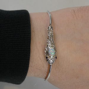 Könnte beinhalten: Ein silbernes Armband mit einem Opal und Rubinen. Das Armband wird am Handgelenk einer Person getragen.