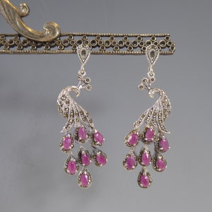 May include: A pair of silver peacock earrings featuring pink gemstones. The earrings are detailed with marcasite stones and have a dangling design.
