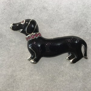 Peut inclure: Broche en forme de dachshund noir avec un collier de strass rouges. La broche est en métal et a une finition brillante.