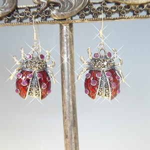 May include: A pair of silver earrings with red enamel ladybug designs. Each ladybug is decorated with small pink gemstones and black marcasite stones.