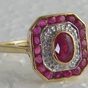 Peut inclure: Une bague en or avec un gros rubis ovale entouré d'un halo de petits diamants et d'une bordure de rubis.
