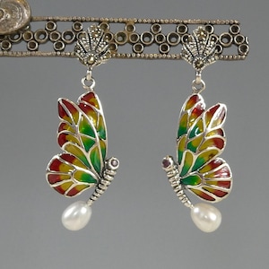 May include: Butterfly earrings with wings in red, yellow, and green enamel. The silver earrings have a pearl drop and are displayed on a decorative silver bar. The earrings are a beautiful piece of jewellery.