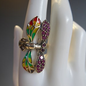 May include: A gold ring with a dragonfly design. The dragonfly's wings are enameled in red, yellow, and green. The dragonfly's body is set with ruby-colored stones.