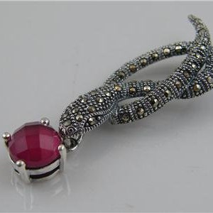 Peut inclure: Une broche en argent en forme de serpent avec une pierre précieuse rouge. Le serpent est fait de marcassite et est enroulé en cercle. La pierre précieuse est un cabochon rond.