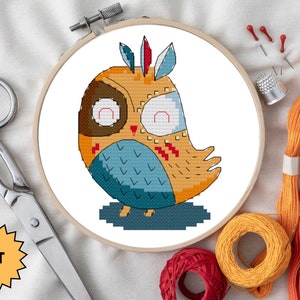 May include: A cross-stitch kit featuring a colorful owl with a brown head, blue wings, and orange body. The owl has a red and white feather on its head. The kit includes embroidery floss, a needle, and a piece of Aida cloth.