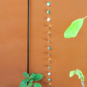 May include: A string of small, round, silver-colored mirrors hangs from a black cord against a brown wall. The mirrors are spaced evenly apart and reflect light.
