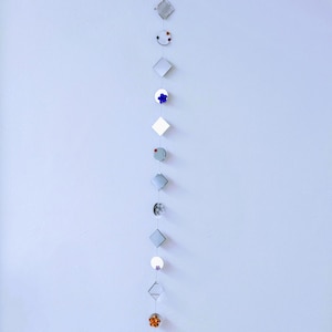 May include: A string of small, square mirrors hangs from the ceiling. Each mirror is decorated with a small, dried flower or leaf. The mirrors are arranged in a vertical line, with the top mirror being the smallest and the bottom mirror being the largest.