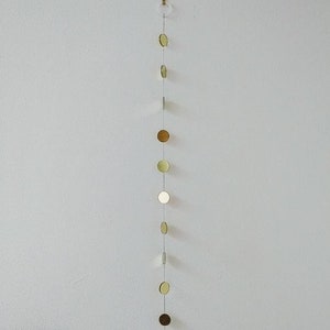 May include: A gold, silver, and white hanging garland of round, mirrored ornaments. The garland is suspended from a white ceiling with a clear plastic hook.