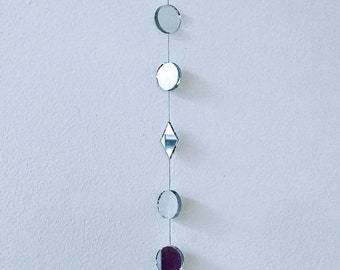 Puede incluir: Un móvil plateado y blanco con una variedad de formas, incluyendo círculos, diamantes y lágrimas, colgando de una cuerda.