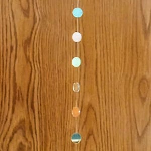 May include: A string of colorful paper circles hanging on a wood background. The circles are in shades of blue, green, white, and orange.