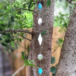 May include: A vertical hanging mobile featuring a series of reflective glass and crystal elements strung together on a thin wire. The strand includes clear circular discs, a diamond-shaped mirror, and two vibrant blue oval-shaped glass beads.