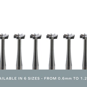May include: Six dental burrs with star-shaped heads are arranged in a row against a white background. The burrs are metallic grey with a cylindrical shaft. The text at the bottom reads "AVAILABLE IN 6 SIZES - FROM 0.6mm TO 1.2mm."
