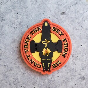 May include: A round, orange patch with the text "CAN'T TAKE THE SKY FROM ME" encircling a black spaceship design on a yellow background. The center features Japanese characters.