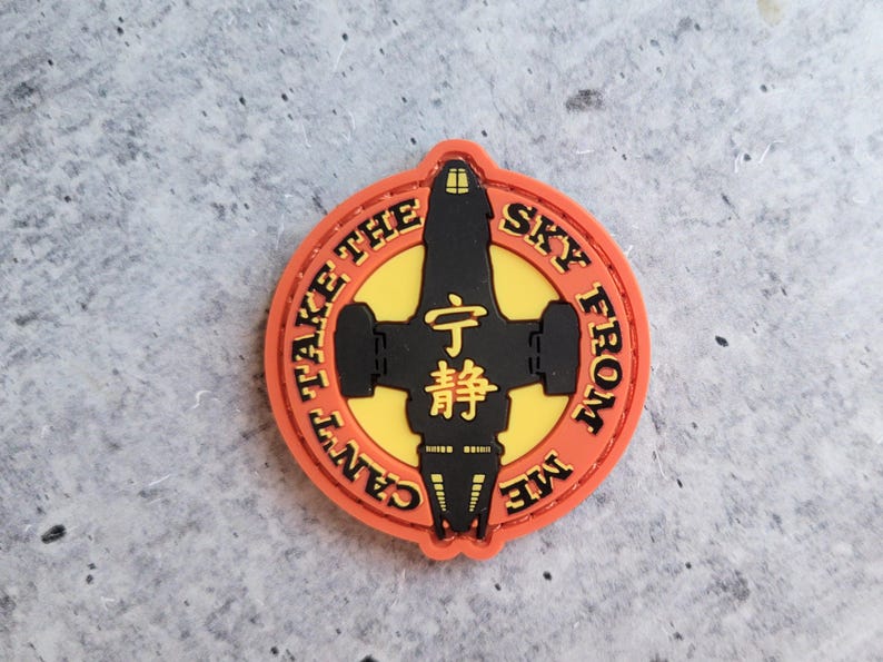 May include: A round, orange patch with the text "CAN'T TAKE THE SKY FROM ME" encircling a black spaceship design on a yellow background. The center features Japanese characters.