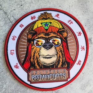 Puede incluir: Parche bordado circular con un oso que lleva gafas de sol, un sombrero y una bufanda roja. El oso es la imagen central, rodeado por un borde blanco con caracteres chinos y las palabras "CALIFORNIA BROWNCOATS" en un letrero de madera.