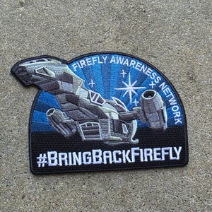 May include: A semi-circular embroidered patch featuring a grey spaceship against a blue sunburst background with white stars. The text reads FIREFLY AWARENESS NETWORK in an arc and #BRINGBACKFIREFLY in white capital letters at the bottom edge.