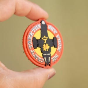 May include: A round, orange, black, and yellow patch with the text "CAN'T TAKE THE SKY FROM ME" and Japanese characters. The patch features a black spaceship design in the center.