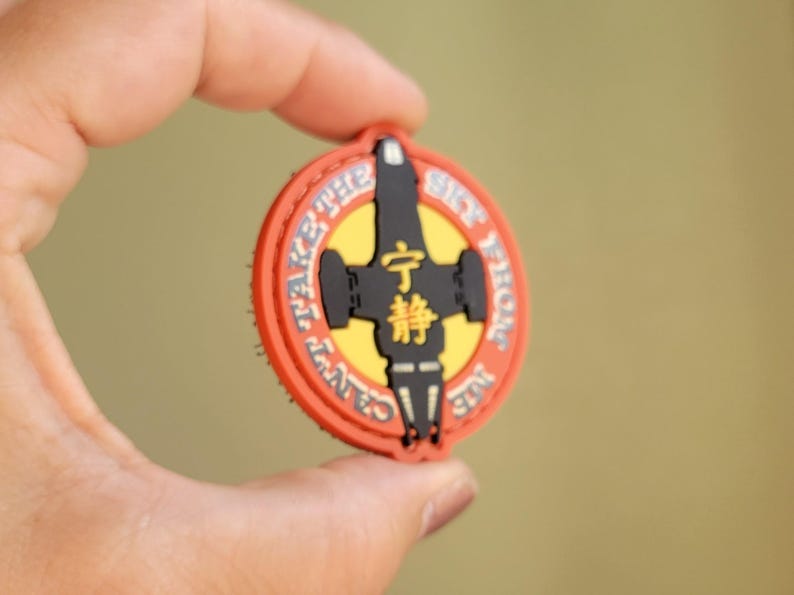 May include: A round, orange, black, and yellow patch with the text "CAN'T TAKE THE SKY FROM ME" and Japanese characters. The patch features a black spaceship design in the center.