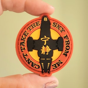 May include: A round, orange and yellow patch with the text "CAN'T TAKE THE SKY FROM ME" encircling a black spaceship design. The center features Chinese characters. A collectible item.