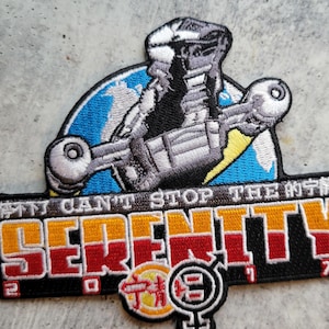 Puede incluir: Parche bordado con una imagen estilizada de una nave espacial y el texto "I Can't Stop The Serenity" y "Serenity 2017". El parche tiene un esquema de color azul, amarillo, rojo y naranja.