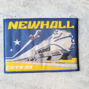 May include: Rectangular patch with a blue background and yellow border. The patch features a stylized train with the text "ACTRANS" and "NEWHALL". Additional text includes "CSTS-29" and a star.