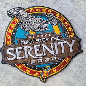 Puede incluir: Parche bordado con un diseño de nave espacial y el texto "CAN'T STOP THE SERENITY 2020". El parche tiene una combinación de colores marrón, azul y amarillo con caracteres chinos alrededor. Un artículo decorativo.
