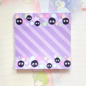 May include: Purple notepad with a striped pattern and a border of black fuzzy creatures with white eyes and pastel coloured flowers and stars.