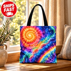 Peut inclure: Un sac fourre-tout avec un motif tie-dye vibrant présentant une spirale orange centrale entourée de vagues tourbillonnantes de couleurs bleu, violet, rose et jaune. Le design inclut un effet de champ d'étoiles sur le tissu et des anses noires.
