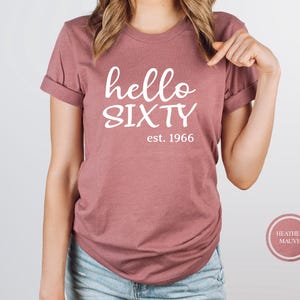 A woman wearing a pink t-shirt with the text "Hello SIXTY" printed on it.