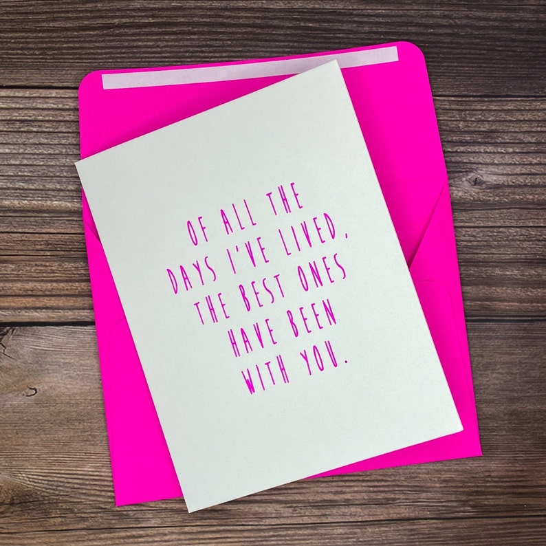 K&ouml;nnte beinhalten: Eine wei&szlig;e Karte mit rosa Text, der lautet: "Von all den Tagen, die ich gelebt habe, waren die besten mit dir." Die Karte liegt auf einer Holzoberfl&auml;che.
