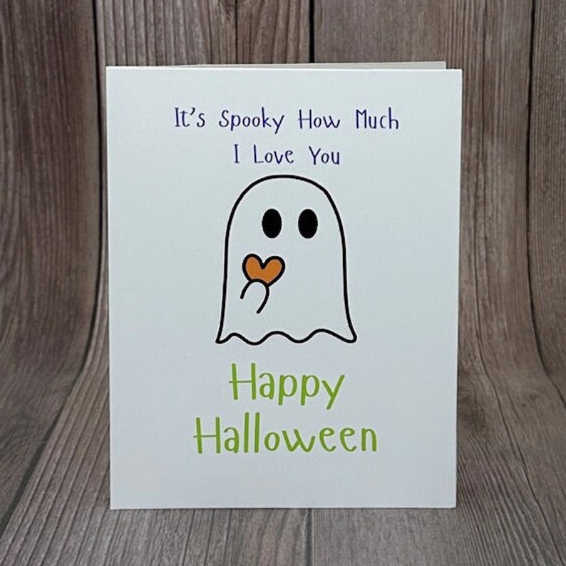 May include: A white card with a ghost illustration and the text "It's Spooky How Much I Love You" in purple. The ghost is blowing a heart and the text "Happy Halloween" is in green.