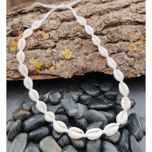 May include: A white shell necklace with a white string. The necklace is on a background of brown wood and black stones.