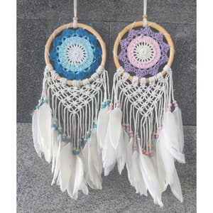 May include: Two white dreamcatchers with wooden hoops and white feathers. One dreamcatcher has a blue and white crocheted centre, and the other has a purple and pink crocheted centre.