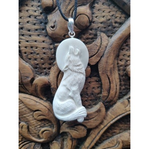 May include: White wolf pendant carved from bone, howling at the moon. The pendant is attached to a black cord.