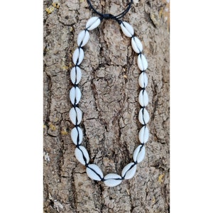 May include: A white shell necklace with black string. The necklace is made of cowrie shells and is strung on a black cord.