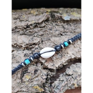 May include: A black cord bracelet with a white cowrie shell charm and turquoise beads.
