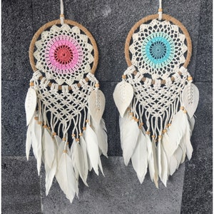 May include: Two white dreamcatchers with white feathers and wooden beads. One dreamcatcher has a pink and white crocheted center, and the other has a blue and white crocheted center.