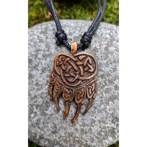 May include: A brown wooden bear paw pendant with a Celtic knot design, hanging from a black cord necklace.