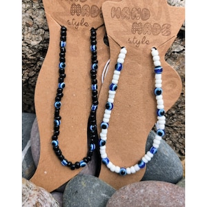 May include: Two beaded bracelets with blue evil eye charms. One bracelet has black beads and the other has white beads. Both bracelets are on brown card stock with the text "Handmade style" printed on them.